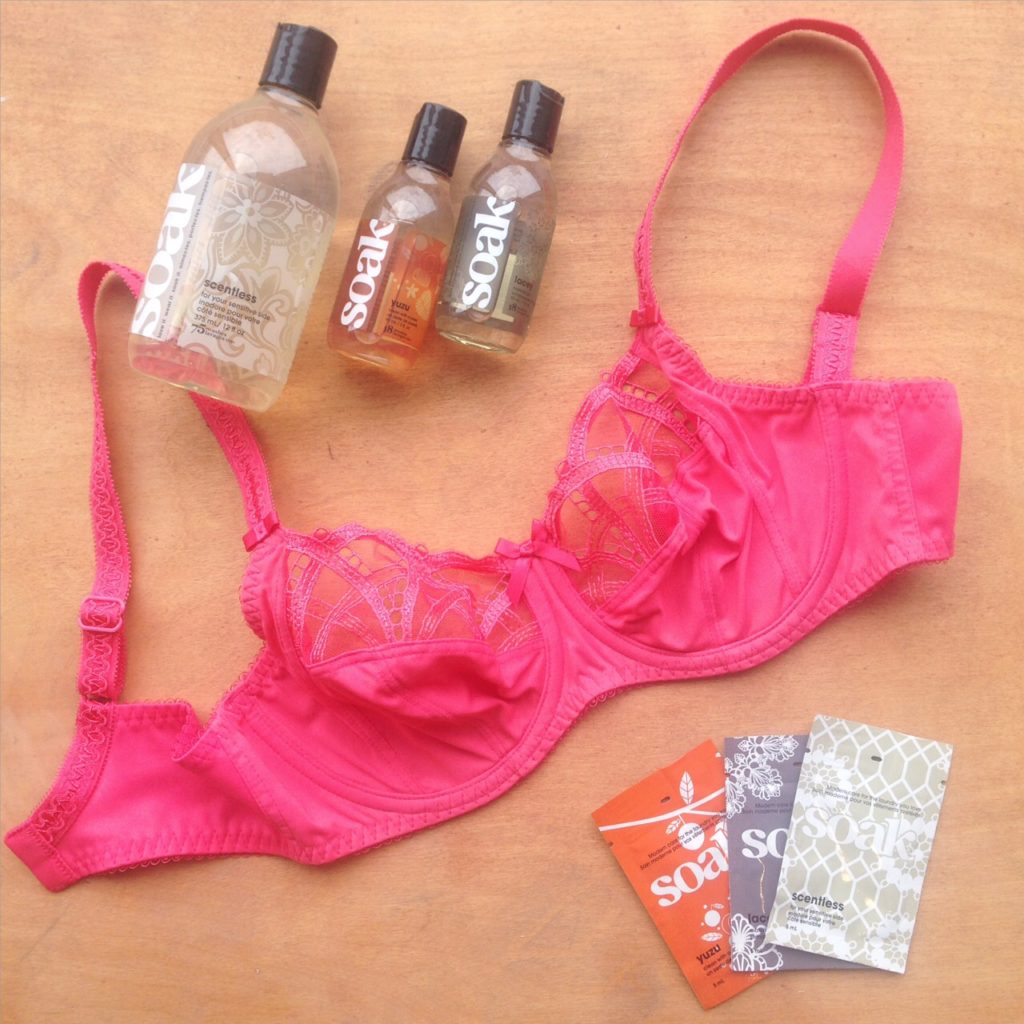 A pink bra, surrounded by bottle of Soak delicates wash