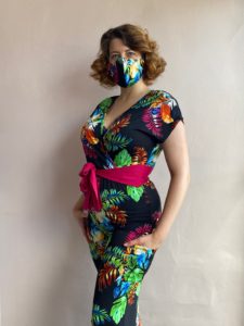Woman standing in tropical jumpsuit and matching mask with her hand in the pocket of the jumpsuit 